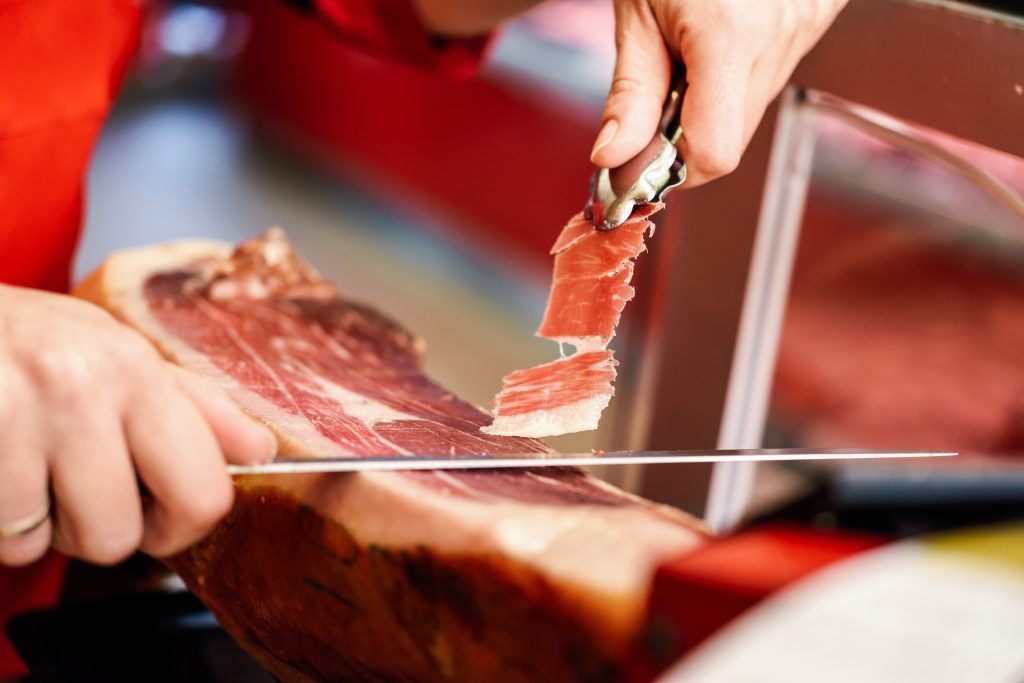 Close up of professional cutter carving slices from a whole bone in serrano ham